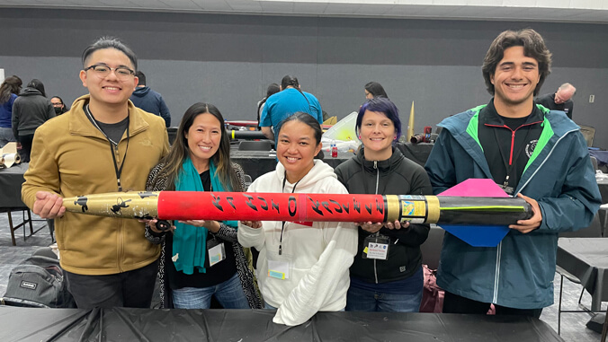 five people standing holding a rocket