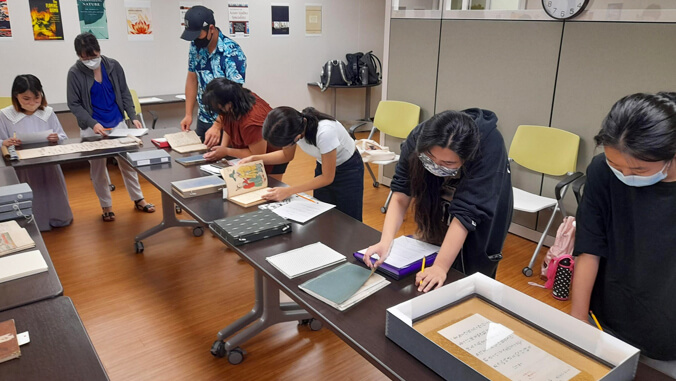 Students standing around desks with books and scrolls