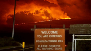 Volcanic eruption in background with "Welcome you are entering Pohakuloa training area" sign