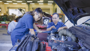 Student working under the hood of a car with an instructor nearby