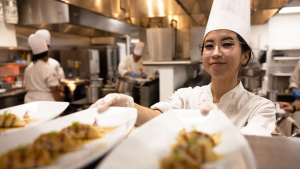 Student in chef hat holding plates of food