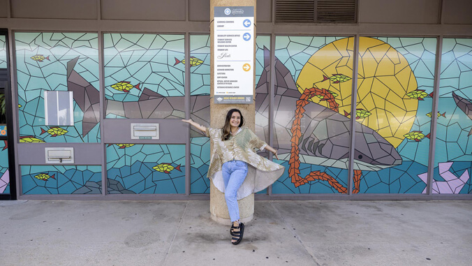 Student artist posing in front of the mural she designed