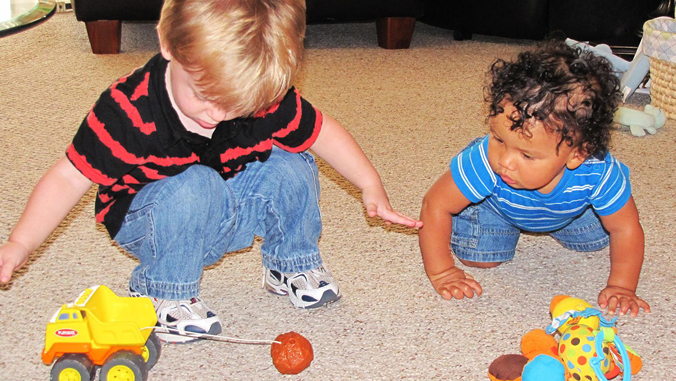 Two toddler-aged children on the floor with toys