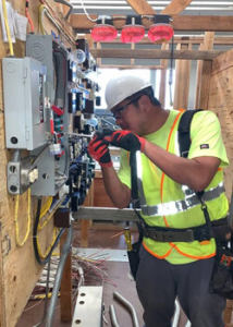 Student in hi-viz vest and hard hat working on an electrical panel