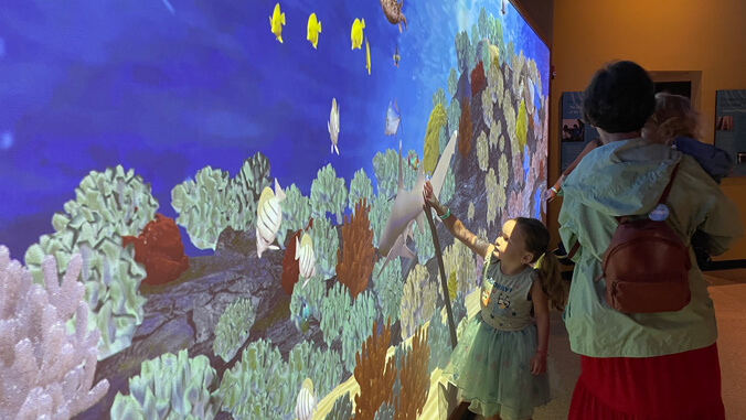 Small child touching a screen featuring the image of a coral reef