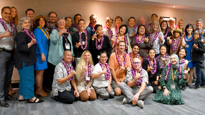 Group of smiling people wearing lei and flashing shaka