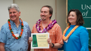 Three smiling people with the center person holding his certificate