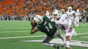 person in a green jersey falling to the ground with a football