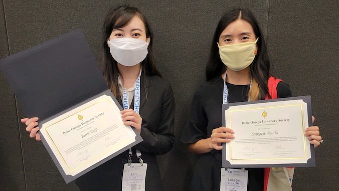 two females holding up certificates with masks on