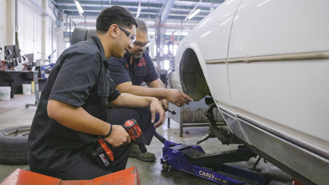 Two people working on the wheel well of a car in a garage