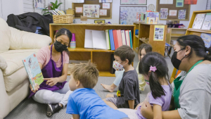 Childcare worker seated on the floor reading to children