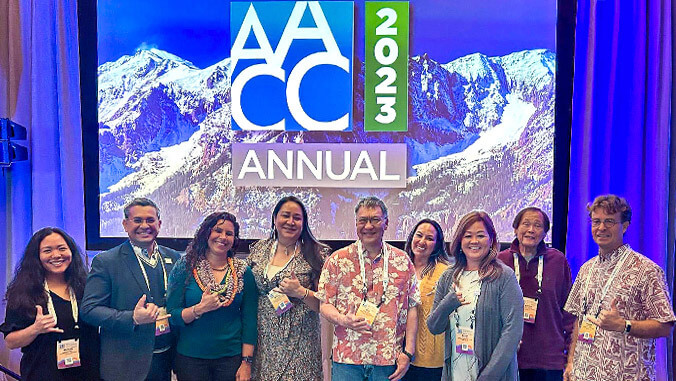group of people standing in front of A A C C screen
