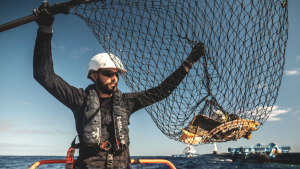 Man in a boat holding a net with plastic debris