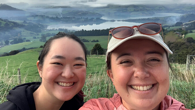 Two smiling students with New Zealand valley and waterway in the background