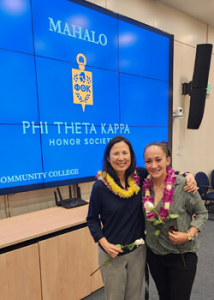 Two people standing in front of a screen with the words "Mahalo Phi Theta Kappa honor society"