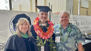 Three people, two wearing graduation regalia and one in aloha shirt