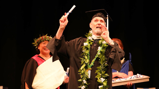 Boom in graduation regalia holding his diploma up high