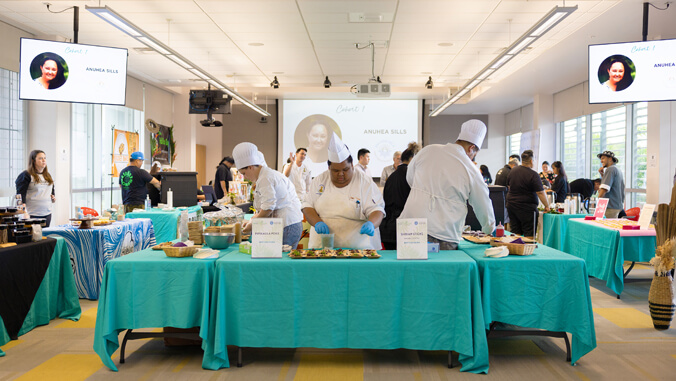 People in culinary outfits preparing food at demonstration tables
