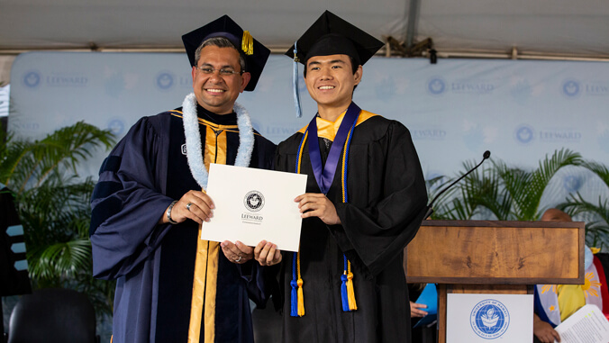Chancellor and graduate at commencement holding a diploma and smiling