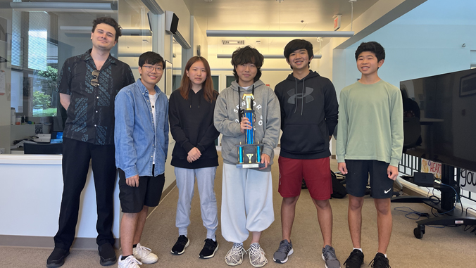 six people standing and smiling with a trophy