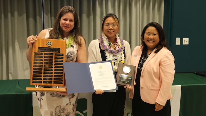 three people smiling holding up awards