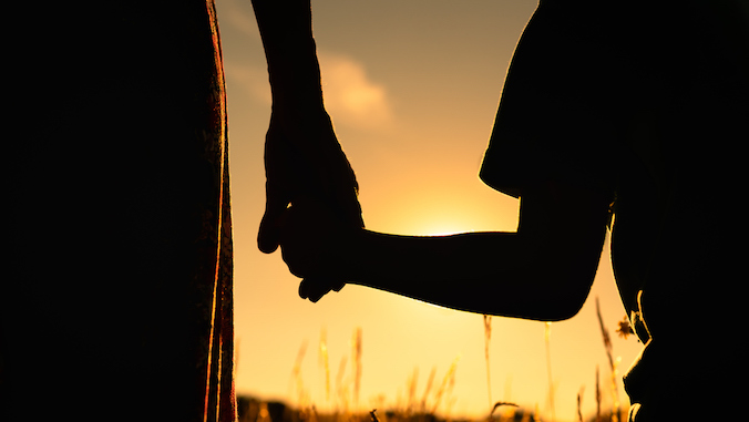 Silhouette of mother and child holding hands facing the sunset 