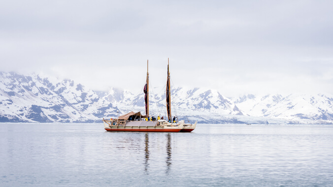 Voyaging canoe passing snow covered mountains