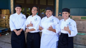 Students in culinary outfits smiling and flashing shaka