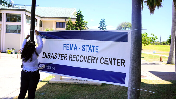 woman tying FEMA Disaster recovery Center sign between 2 trees