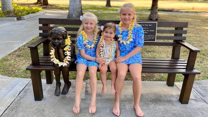 three girls sitting on bench next to statue