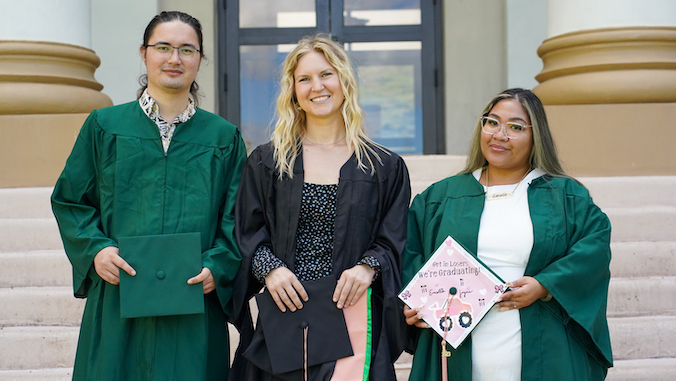 three students in grad gowns