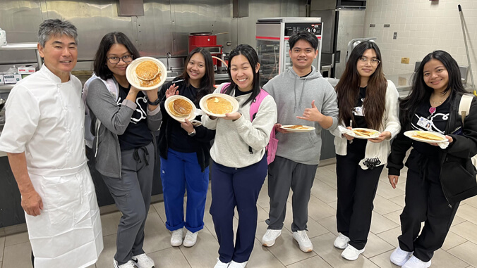 Students holding plates of pancakes with Chef Roy Yamaguchi