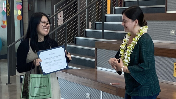 woman holding certificate, another woman wearing lei