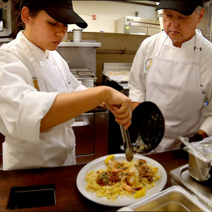 Two culinary students plating a pasta dish