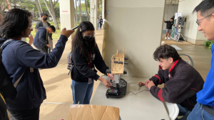 people measuring the load capability of a popsicle bridge