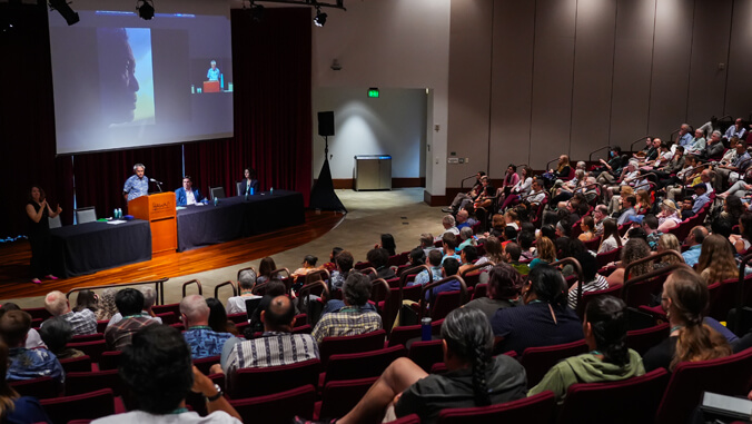 person speaking on podium in front of a crowd of people