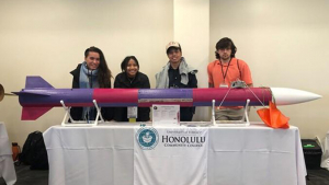 Four students standing behind a rocket