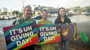 Three smiling people holding Giving Day signs