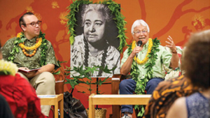 2 people talking with Pukui’s photo behind them
