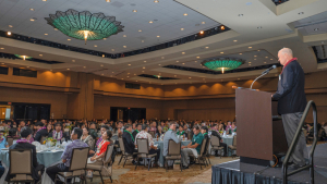 person speaking at a podium in front of a large ballroom