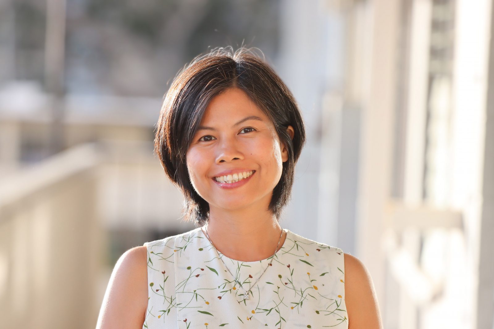 Ph.D. Candidate (ABD as of July 2022) Hoa Le's headshot. Neck-length haircut with black hair and side-swept bangs, slightly tan, and smiling. Wearing a white sleeveless top.