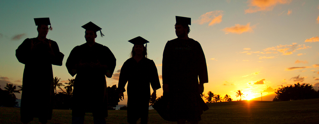 Silhouettes of four students in graduation regalia walking into the sunset